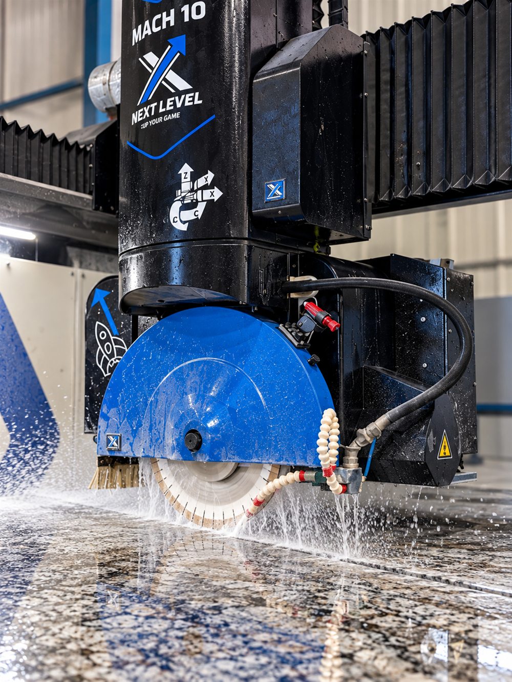 A CNC bridge saw cutting a granite slab with water spray in the Dover Stone shop